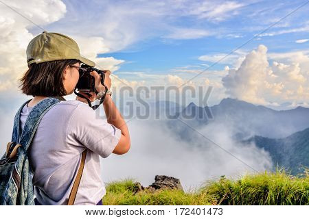 Hiker asian teens girl with digital camera and backpack taking photo beautiful natural of sierra sky clouds and fog during sunset in winter on mountain at Phu Chi Fa Forest Park Chiang Rai Thailand