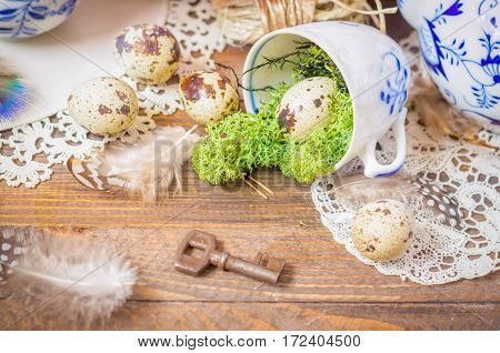 Spring floral still life with blue cup, moss. Lantern, feathers and quail eggs on wooden background