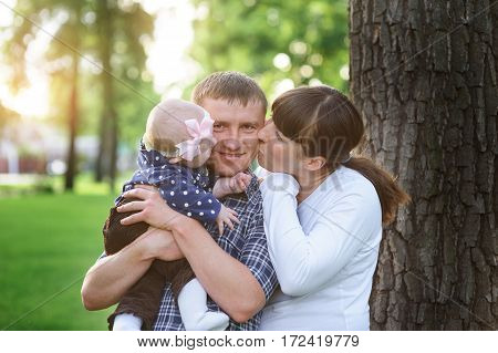happy family in the park in spring sunny day kissing of daddy.