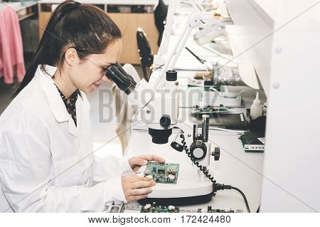 Beautiful female computer expert professional technician examining board computer in a laboratory in a factory. Troubleshooting. Technical support. Engineering. Manufacturing.