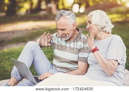 Distance call. Positive delighted senior couple looking at the laptop screen and greeting their children while making a distance call