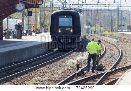 HASSLEHOLM SWEDEN - MAY 05 2016: Tracklayer working with the railroad when a train is arriving to the train station. May 05 2016 Hassleholm Sweden