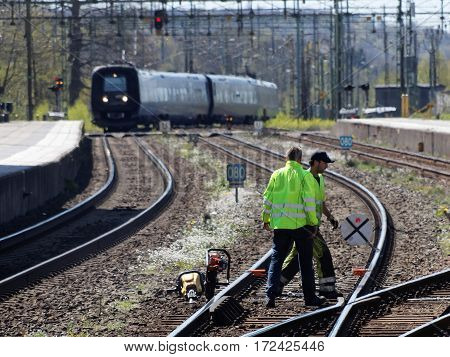 HASSLEHOLM SWEDEN - MAY 05 2016: Tracklayer working with the railroad when a train is arriving to the train station. May 05 2016 Hassleholm Sweden