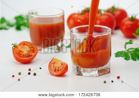 Two glasses of tomato juice with tomatos on white background.