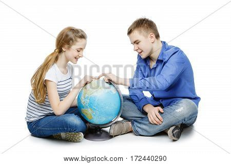 Beautiful teen boy and girl in casual clothes sitting on floor looking for something on the Earth globe. Isolated on white background. Copy space.