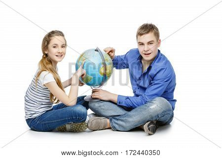 Beautiful teen boy and girl in casual clothes sitting on floor looking for something on the Earth globe. Isolated on white background. Copy space.