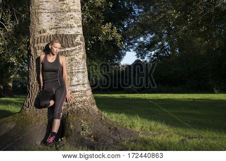 pretty young woman leaning against tree in park to cool down after running