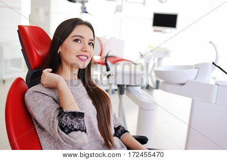 attractive girl in red dental chair at the reception of dentists. Dentistry, teeth whitening, dental fillings, smile, tooth decay.