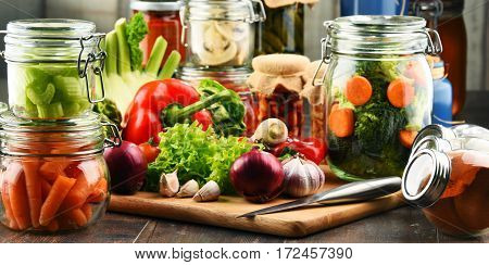 Jars With Marinated Food And Raw Vegetables On Cutting Board