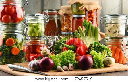 Jars With Marinated Food And Raw Vegetables On Cutting Board