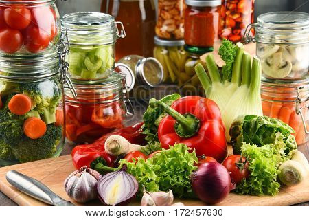 Jars With Marinated Food And Raw Vegetables On Cutting Board