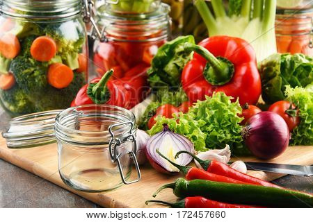 Jars With Marinated Food And Raw Vegetables On Cutting Board