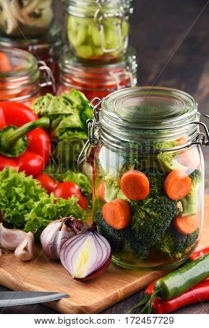 Jars With Marinated Food And Raw Vegetables On Cutting Board