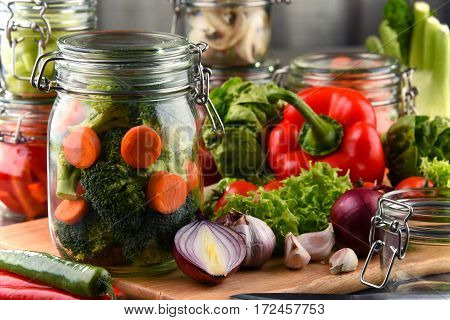 Jars With Marinated Food And Raw Vegetables On Cutting Board