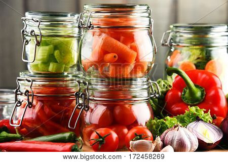 Jars With Marinated Food And Raw Vegetables On Cutting Board