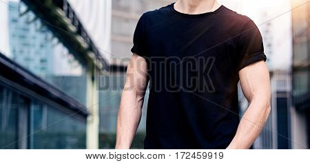 Young caucasian muscular man wearing black tshirt and jeans posing on the street of the modern city. Blurred background. Hotizontal wide mockup
