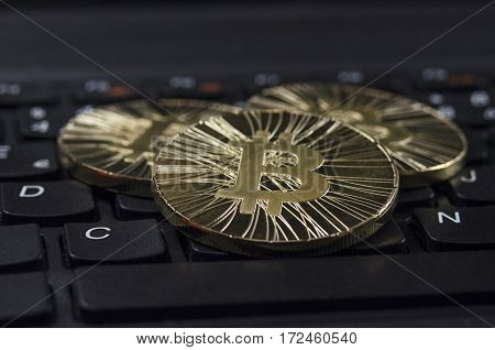 Shiny gold Bitcoin coin laying on black keyboard