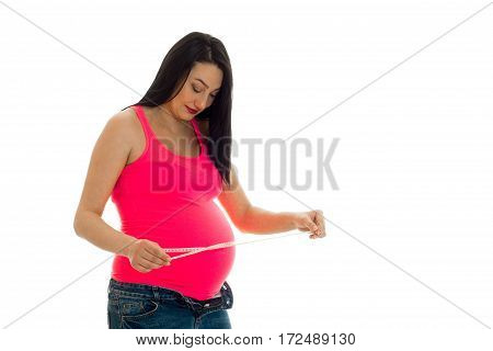 a pregnant young woman holding a measuring Roulette and looking down isolated on white