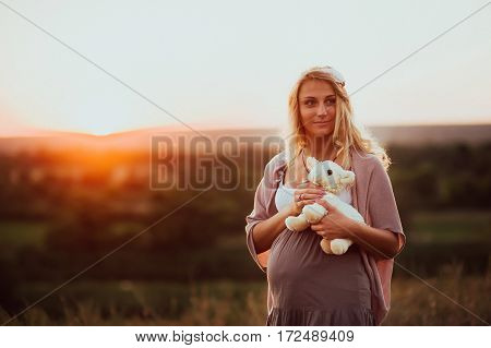 the pregnant girl with a hat in the field of wheat on a sunset