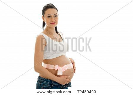 a young pregnant woman stands sideways with a Ribbon on the stomach isolated on white