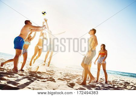 Group of friends is playing beach voleyball at sunset time