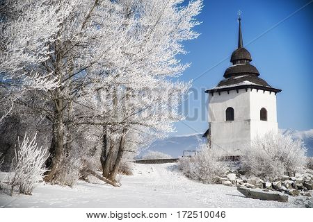 Frost on trees and tower of church. Blue sky