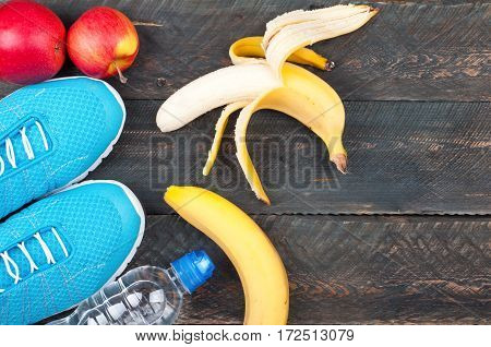 Sport and healthy life. Sport shoes apples bananas and bottle of water on a rustic wooden background. Sport equipment. Conceptual photo. Top view