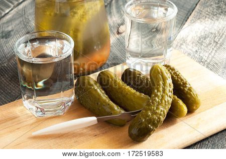 Pickled cucumbers and shot glass of vodka on wooden background. Rustic style