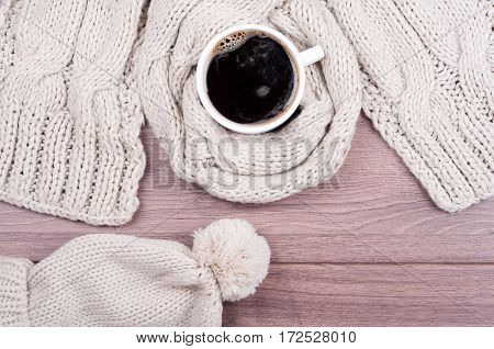 Handmade knitted wool scarf and cap. Winter clothes. Hot coffee cup on wooden background. Concept cozy atmosphere with a cup of coffee in winter. Top view