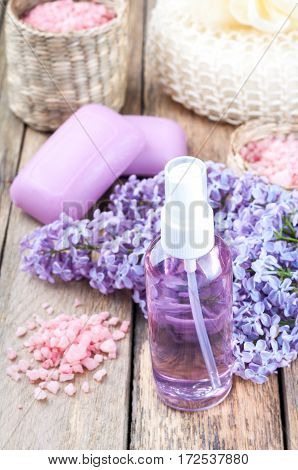 Spa background with blossoming lilac flowers and bottle of essential oil or flower hydrolat cosmetic aroma soap sea salt and accessories
