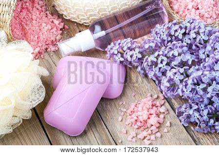 Spa background with blossoming lilac flowers and bottle of aroma oil or flower hydrolat cosmetic soap sea salt and accessories