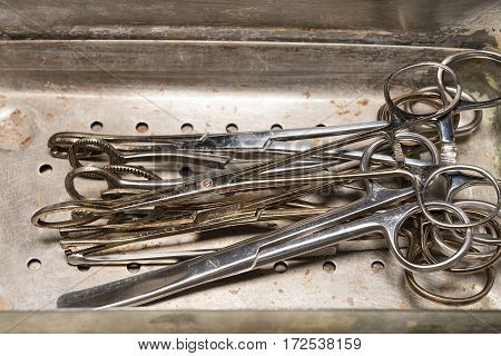 Old forceps and medical scissors in steel tray. Medical equipment. Macro shot.