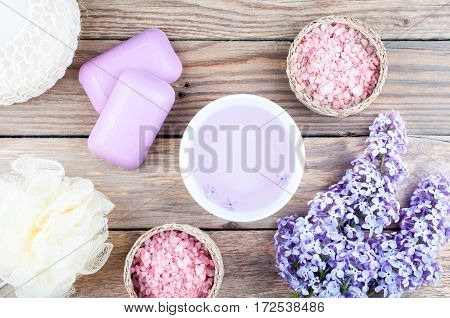 Spa background with blossoming lilac flowers and bowl with essential oil or flower hydrolat aroma cosmetic soap sea salt and accessories