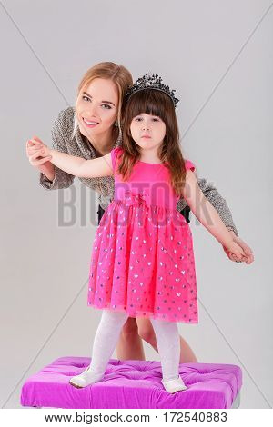 beautiful little girl in pink Princess dress with a crown and beautiful mother hugging on a gray background.