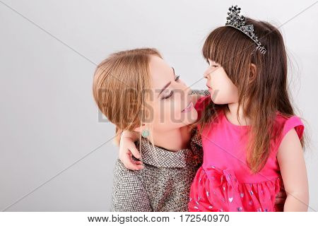 beautiful little girl in pink Princess dress with a crown and beautiful mother hugging on a gray background.