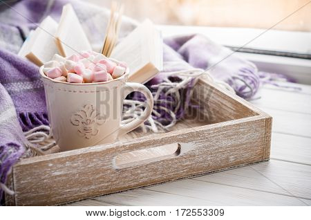 Coffee cup open book marshmallow and plaid on a window sill in winter. Concept warm and cozy home decor. Vintage style
