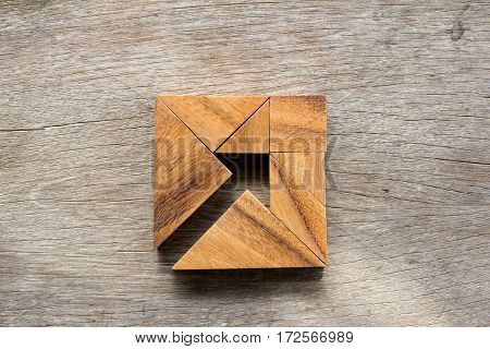 Tangram puzzle as arrow in square shape on wooden background (Concept for business direction and decision)