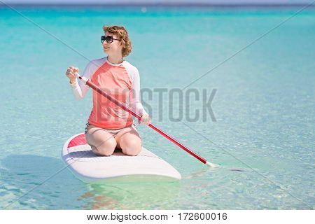 young woman in rashguard enjoying stand up paddleboarding at beautiful caribbean lagoon active vacation concept