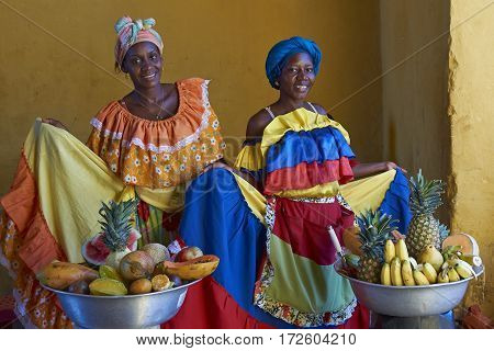 CARTAGENA DE INDIAS, COLOMBIA - JANUARY 24, 2017: Women in traditional costume posing for a photograph whilst selling fresh fruit in the historic walled city of Cartagena de Indias in Colombia