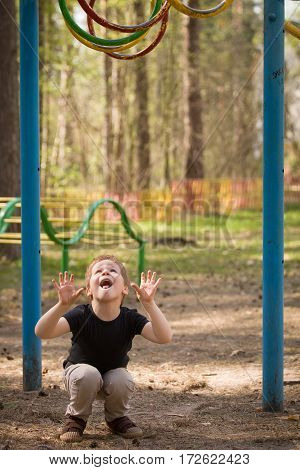 Portrait of cute kid boy jumping on the climbing frame. Young boy climbing on playground during summer. Child enjoys climbing in a children's playground outdoors.