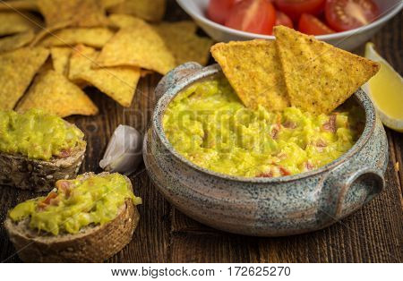 Guacamole in home crafted bowl with tortilla chips on natural wooden desk.
