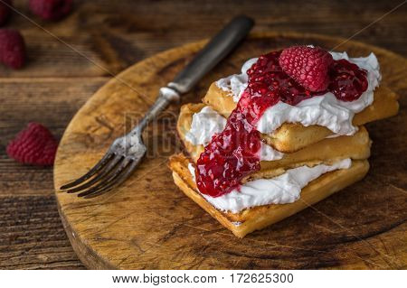 Belgian waffles with raspberries and double cream on rustic table.