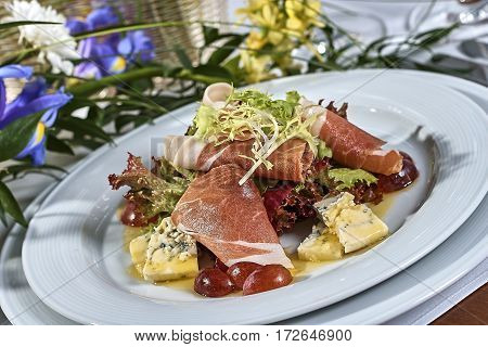 meat salad with ham cheese lettuce Dorblu grapes and olive oil served on a plate on a table with flowers