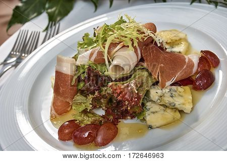 meat salad with ham cheese lettuce Dorblu grapes and olive oil served on a plate on a table with flowers