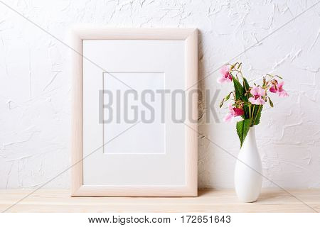 Wooden frame mockup with purple wildflowers in elegant vase. Empty frame mock up for presentation design.