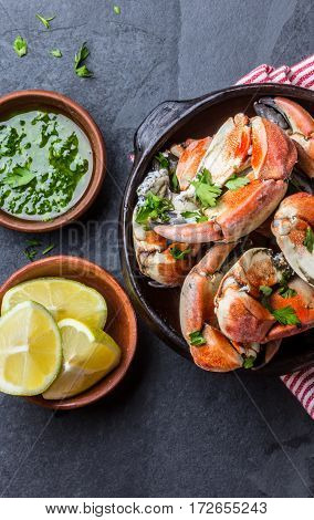 Seafood. Crabs tentacles on clay bowl with lemon and herbs sauce on slate background. Top view