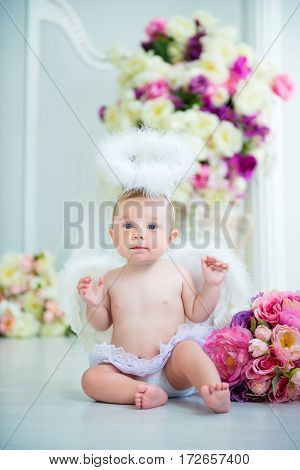 Little angel smiling and happy sitting on the background of flowers and harp.