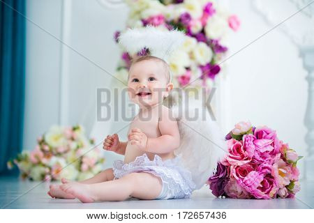 Little angel smiling and happy sitting on the background of flowers and harp.