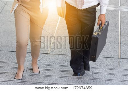 Businessman and Business woman walking up stairs with bags to office.