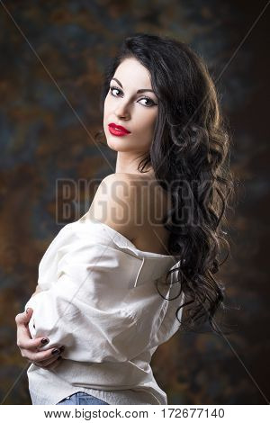 Closeup portrait of young brunette woman in white shirt, dark studio wall background